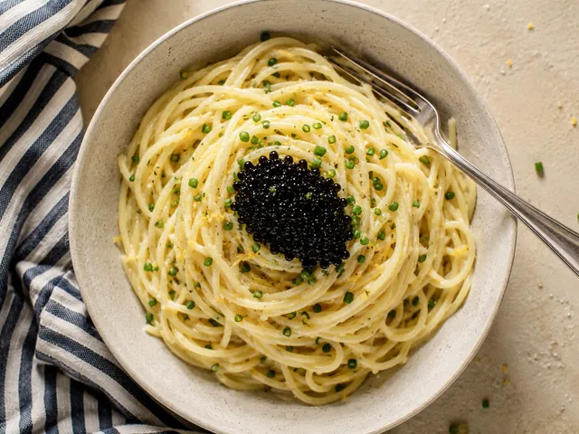 A bowl of buttery lemon spaghetti topped with a mound of black caviar and chives, a fork resting in the bowl.